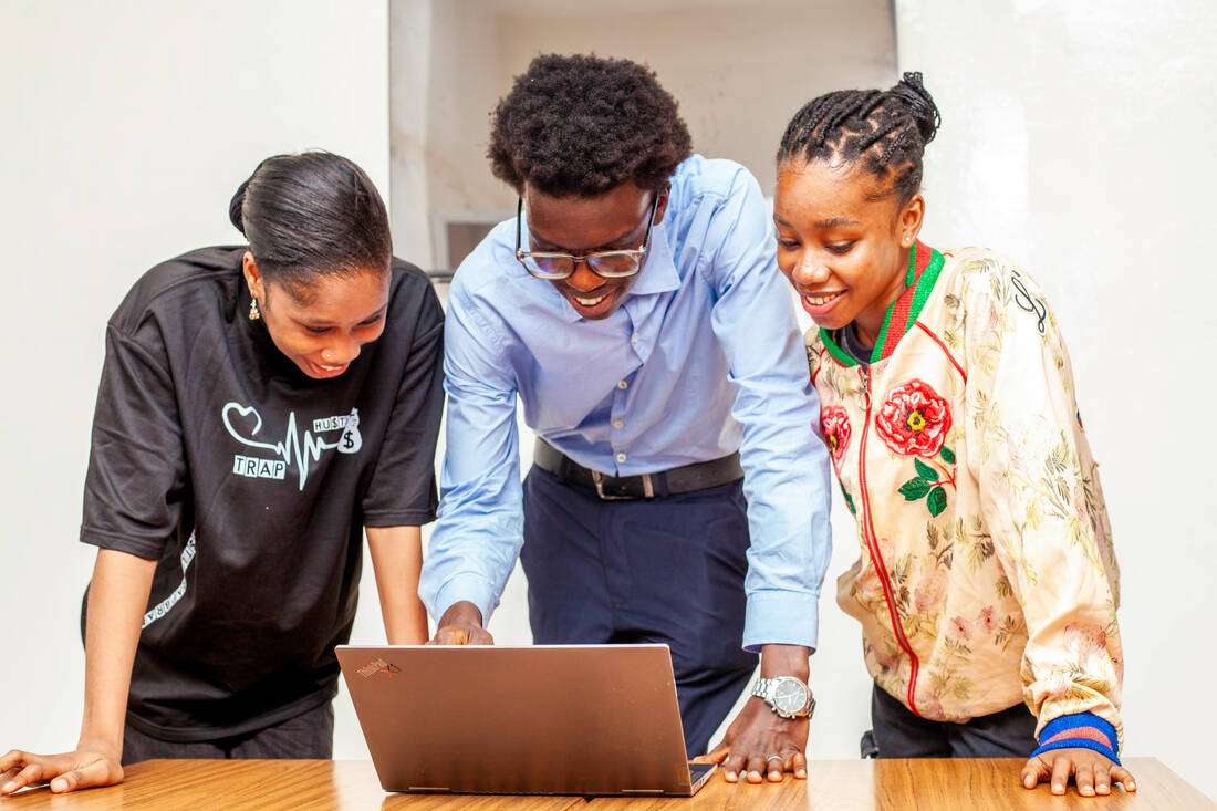 Young people gathered around a laptop, smiling