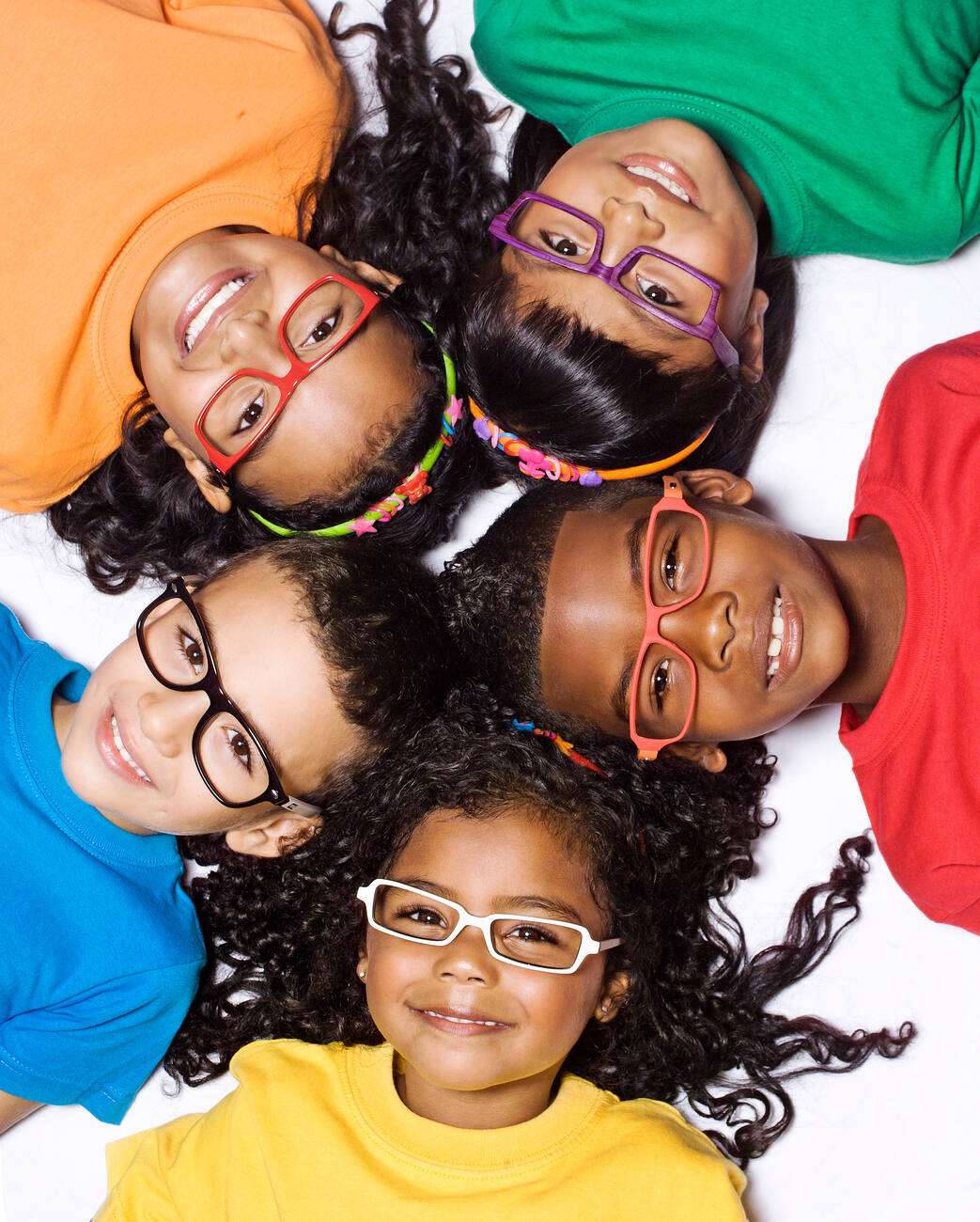 Smiling children in colourful shirts and glasses lying in a circle, heads together