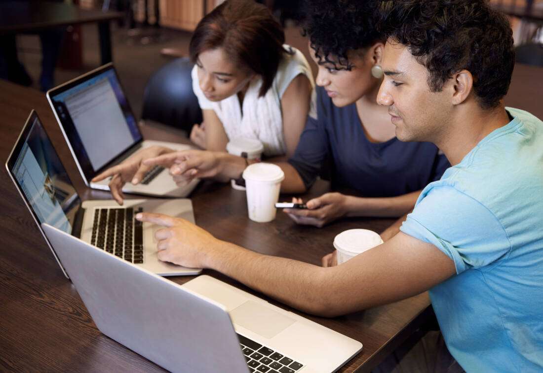 Three adults working together on laptops at a table