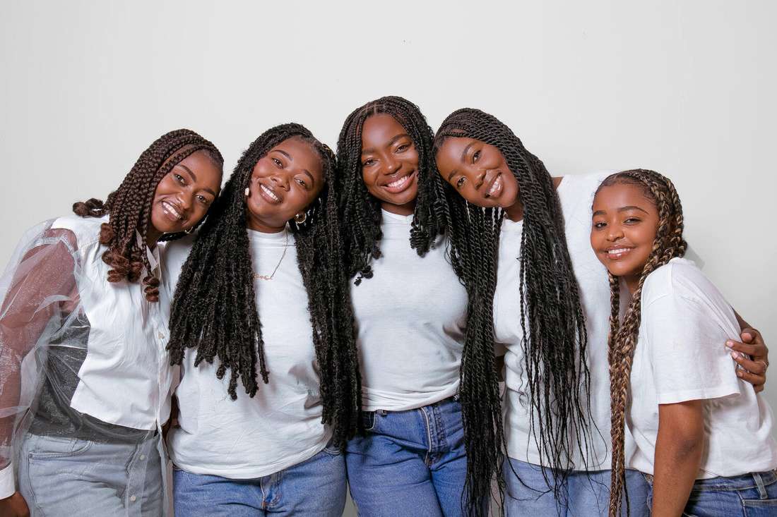Five young Black women with long braids leaning into one another and smiling