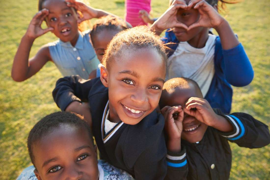 A group of joyful Black children crowding close to the camera, smiling and making heart shapes with their hands