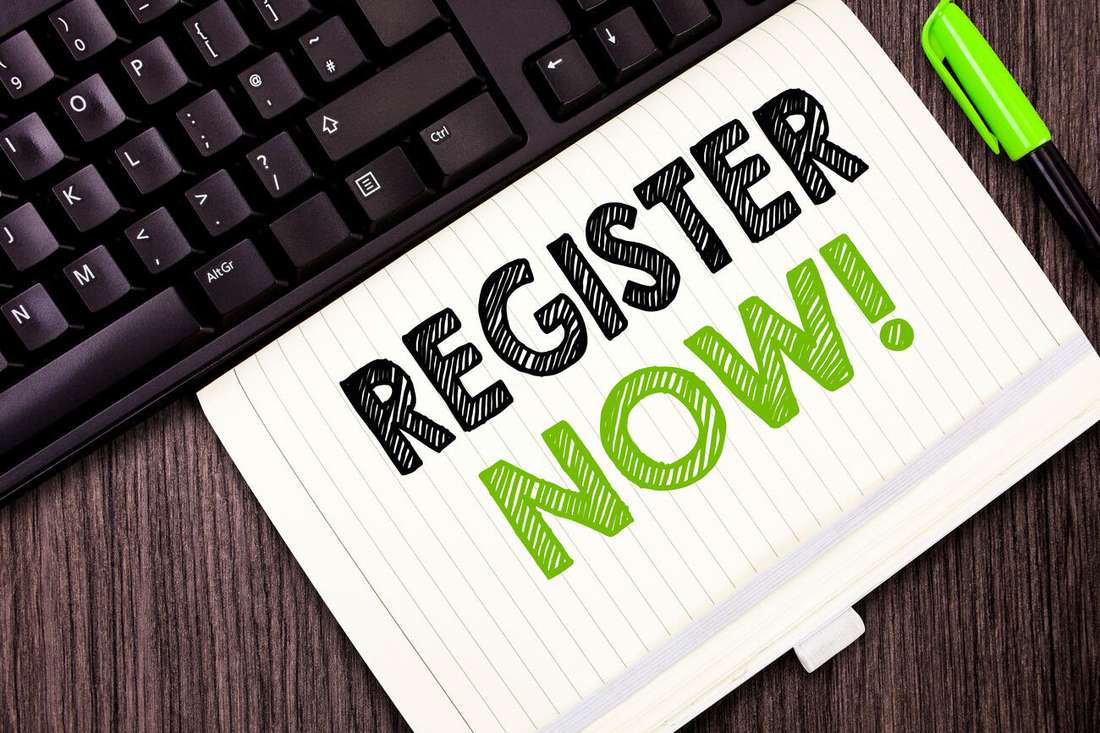 A notebook with the words Register now written in black and green beside a keyboard