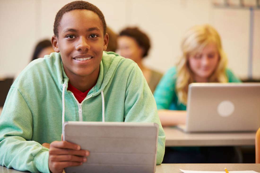 A smiling young man holding a tablet in class