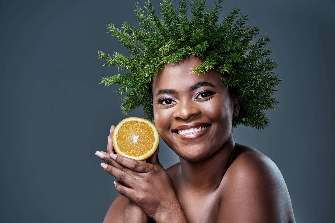 A joyful woman with greenery in her hair holding an orange slice