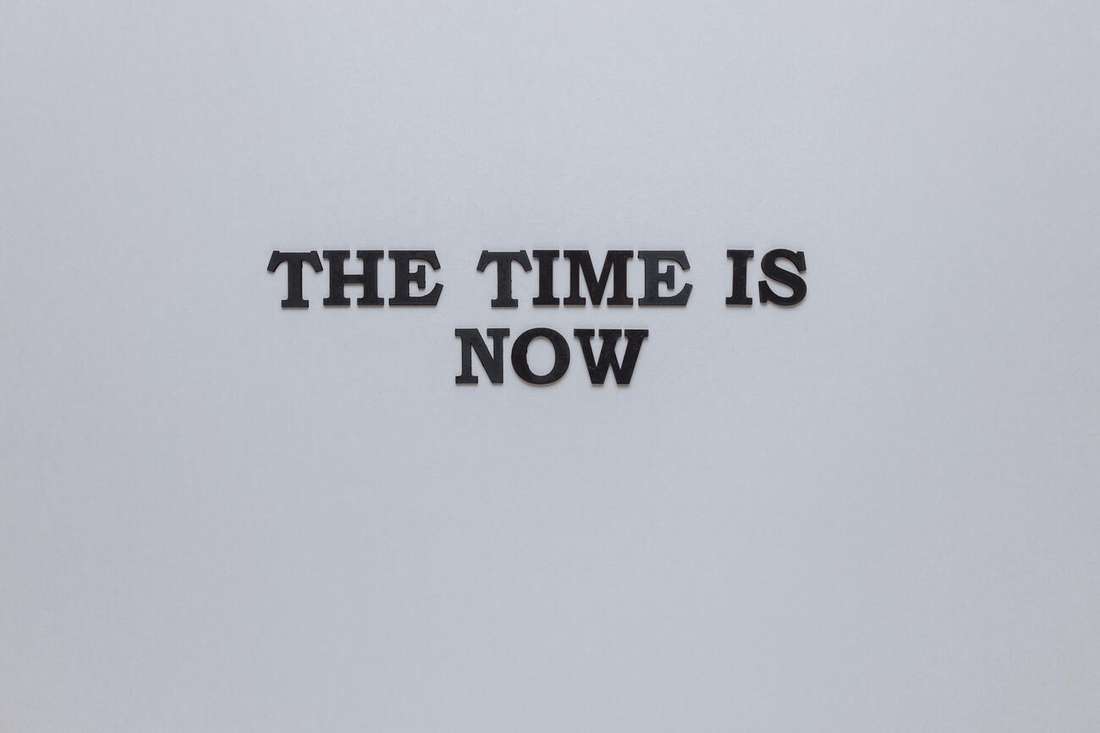 Letters spelling The time is now on a grey background