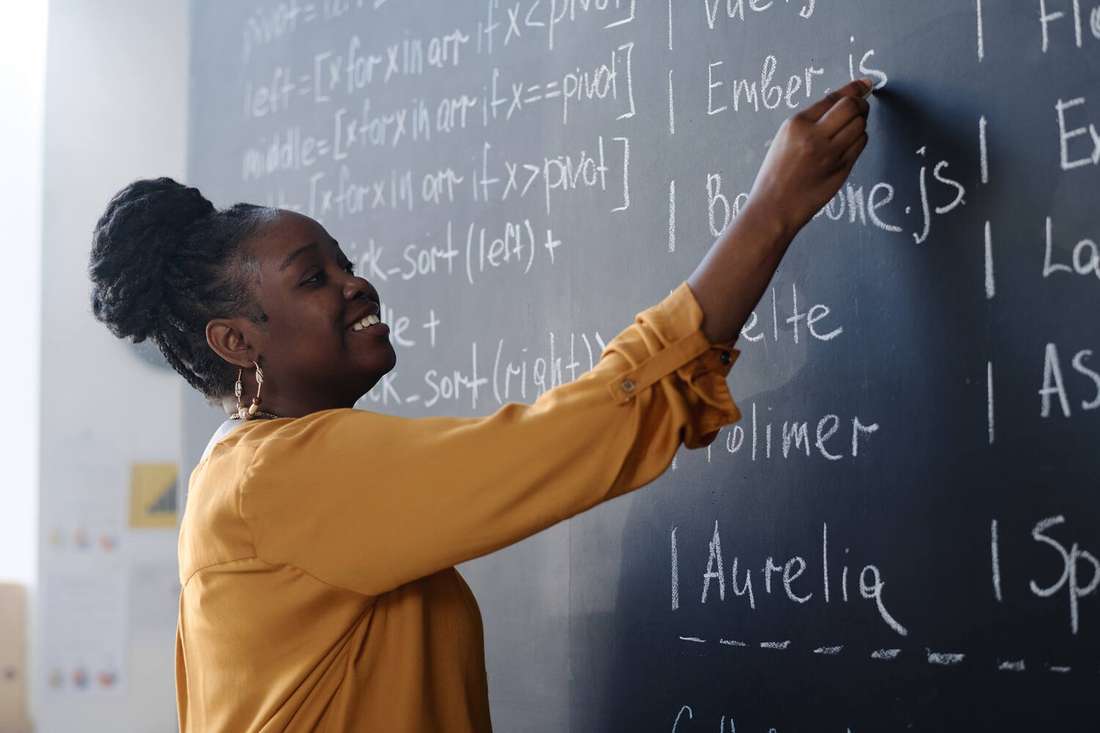 A smiling Black woman teacher writing on a chalkboard
