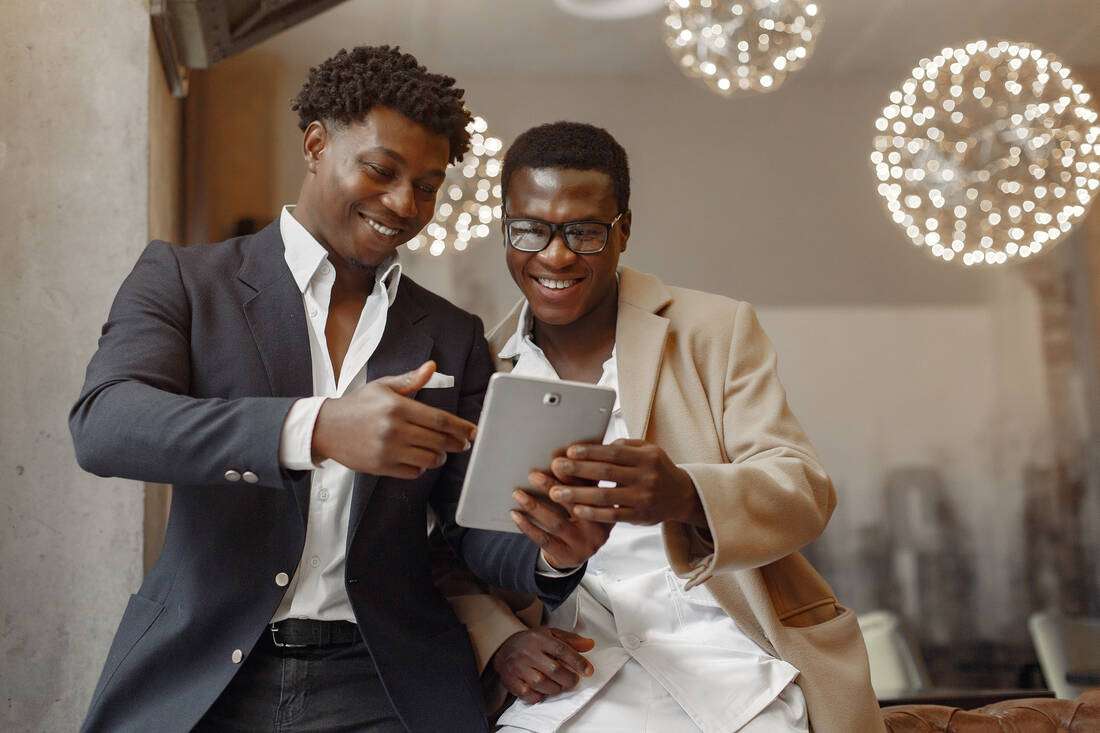 Two smiling young men in suits looking at a tablet together