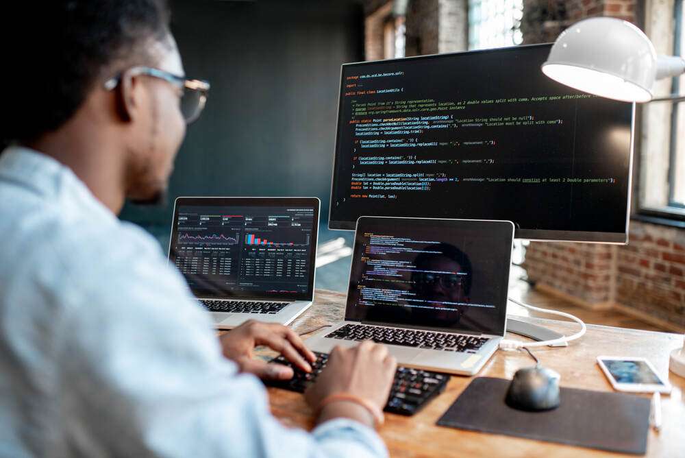 A man working on code across several computer screens