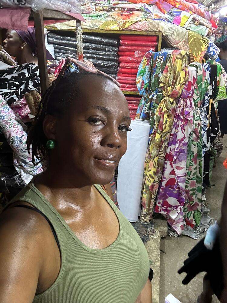 Kathy smiling at a fabric market in Ghana, surrounded by colourful printed fabrics