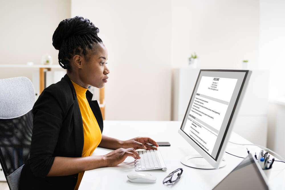 A woman at her desk reviewing her resume on a computer screen