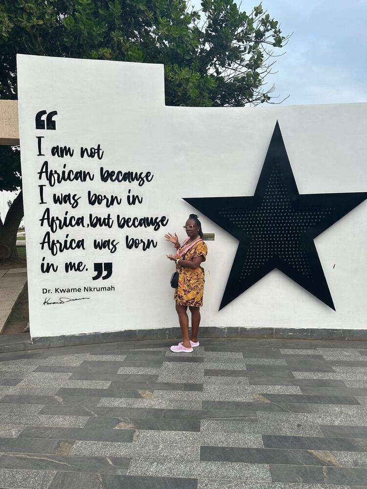 Kathy at the Kwame Nkrumah memorial wall in Ghana, beside a large black star and his words: I am not African because I was born in Africa, but because Africa was born in me