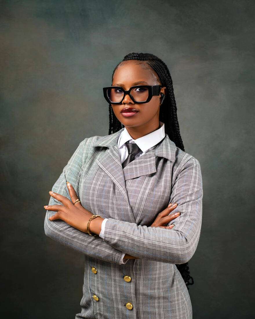 A confident young woman in glasses and a plaid suit, arms crossed
