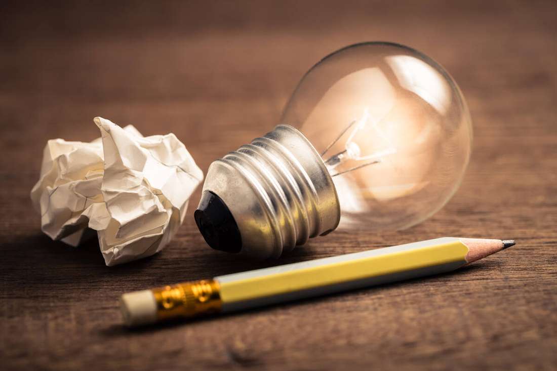 A light bulb, a pencil and crumpled paper on a wooden table